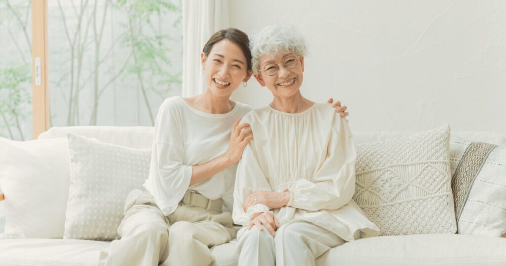 高齢女性と娘が肩を寄せ合って微笑み合っている